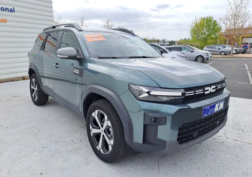 Vue 3/4 avant droit du Dacia Bigster vert cèdre avec jantes bicolores et calandre moderne, stationné en extérieur.