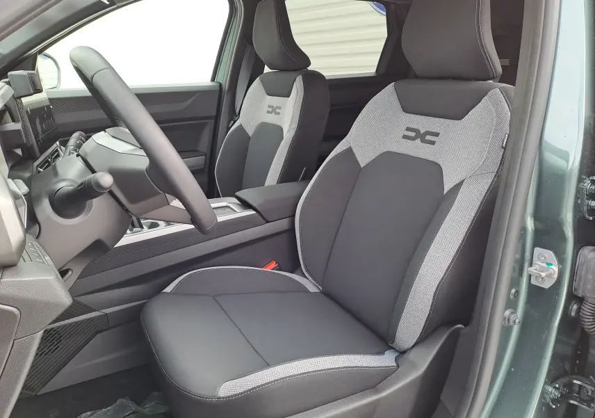 Vue intérieure côté conducteur du Dacia Bigster Hybrid 155 en vert cèdre, avec sièges bi-ton gris et noir au logo distinctif.