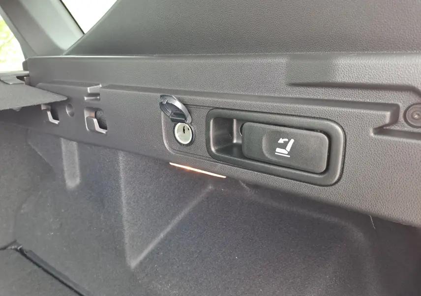 Gros plan sur la commande de rabattement des sièges dans le coffre du Dacia Bigster vert cèdre, version hybride 2026.