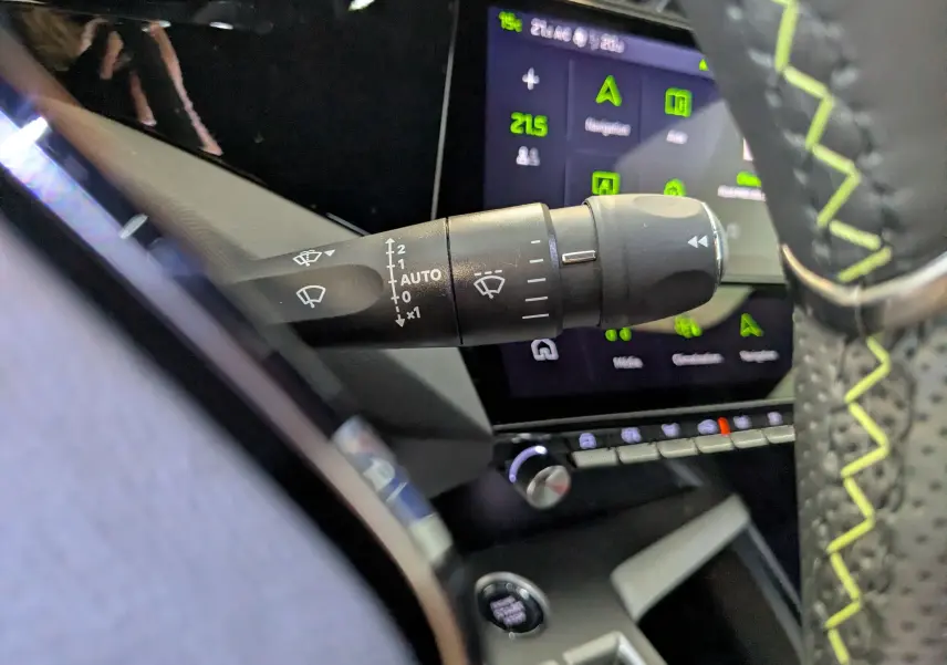 Gros plan sur la commande d’essuie-glace à gauche du volant perforé avec surpiqûres vertes dans un Peugeot 408 Hybrid 2025.