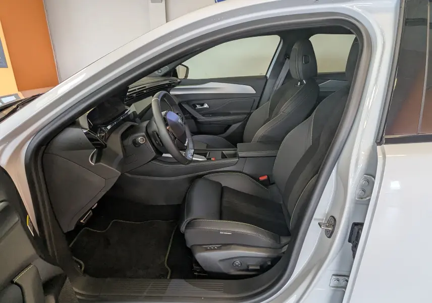 Vue intérieure côté conducteur du Peugeot 408 Hybrid blanc Okenite, sièges noirs en tissu et Alcantara avec surpiqûres vertes.