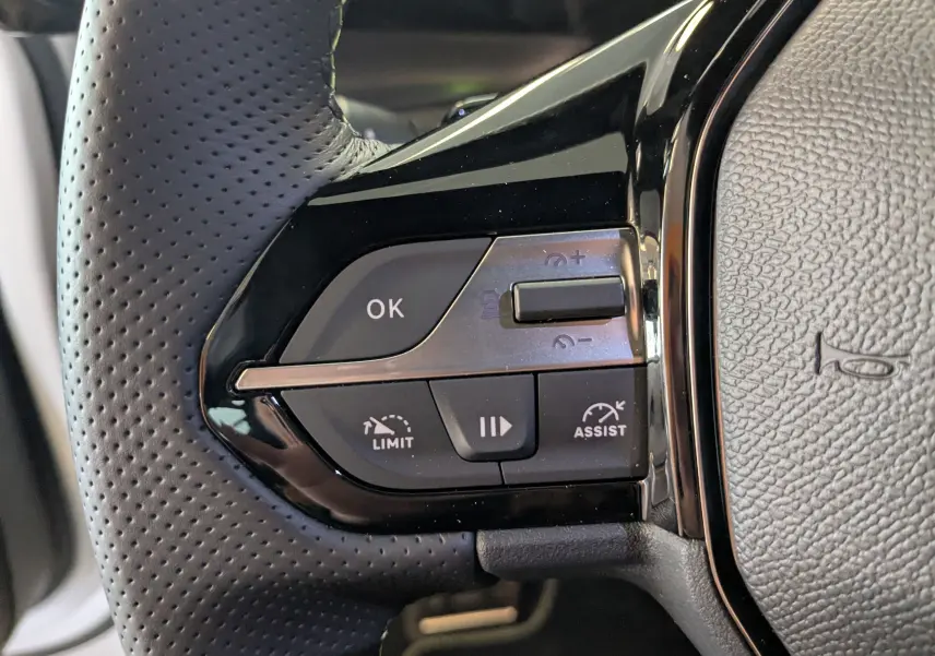 Gros plan sur les commandes gauche du volant noir perforé du Peugeot 408 Hybrid 145 GT, boutons de régulateur et assistant.
