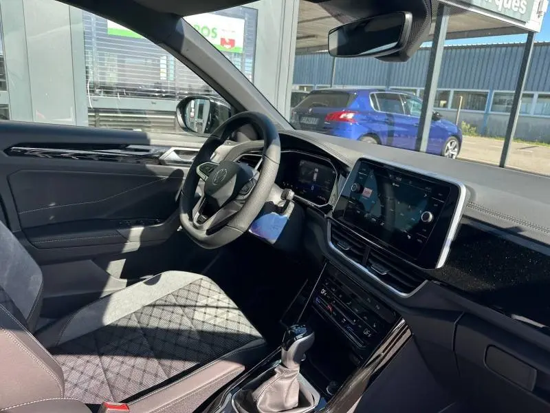 Intérieur avant droit du Volkswagen T-Roc 2025 noir nacré, volant cuir multifonction et écran tactile central visible.
