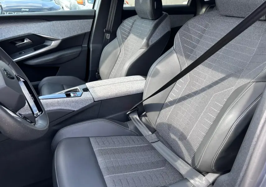 Vue intérieure côté conducteur du Peugeot 3008 Hybrid 136 e-DCS6 GT 2025, sièges gris clair avec cuir et tissu, accoudoir central.