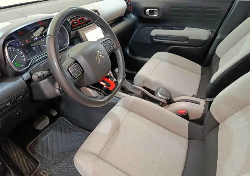 Vue intérieure côté conducteur de la Citroën C3 Aircross beige, avec volant cuir et sièges tissu clair à motifs carrés.