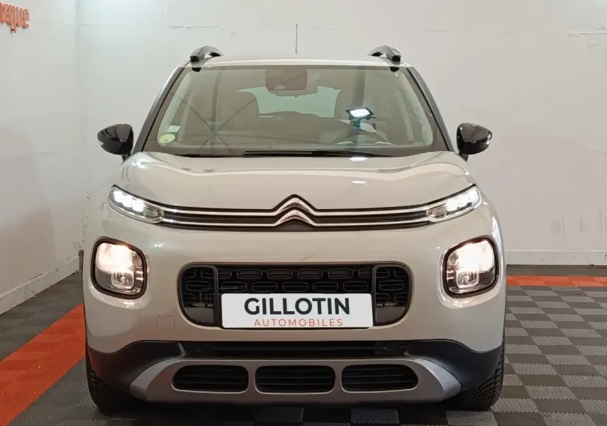 Citroën C3 Aircross beige vue de face, avec calandre noire et feux avant allumés en intérieur showroom.