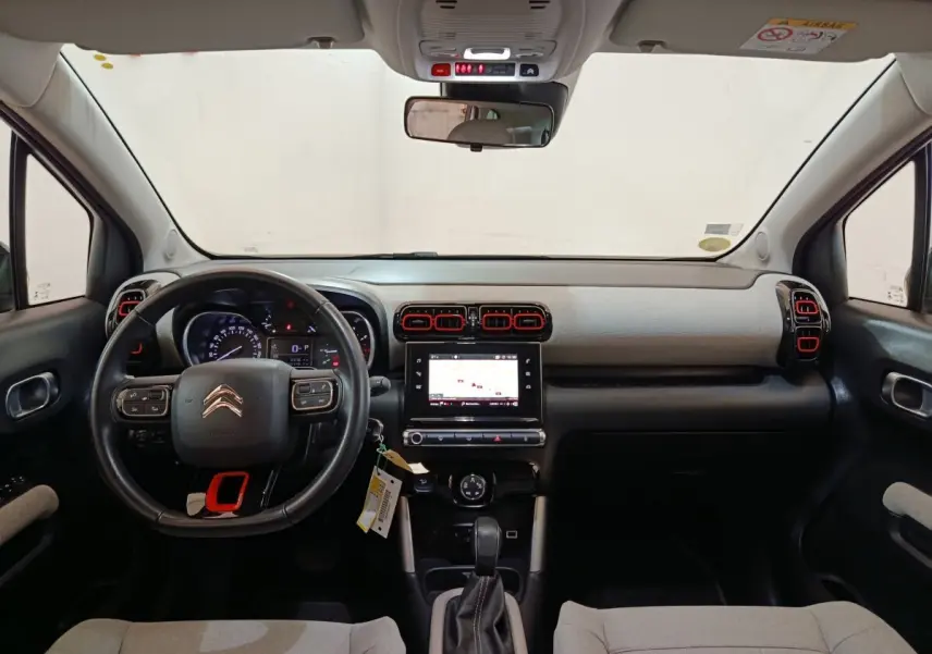 Vue intérieure frontale du tableau de bord de la Citroën C3 Aircross 2021, avec volant cuir noir et touches rouges sur aérateurs.