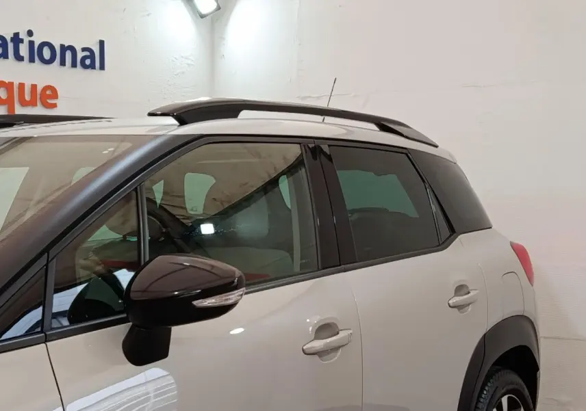 Vue latérale gauche d'un Citroën C3 Aircross beige avec toit et rétroviseur noir, dans un espace intérieur.
