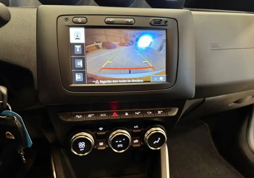 Vue rapprochée du tableau de bord du Dacia Duster 2020 montrant l'écran de caméra de recul et les commandes de climatisation.