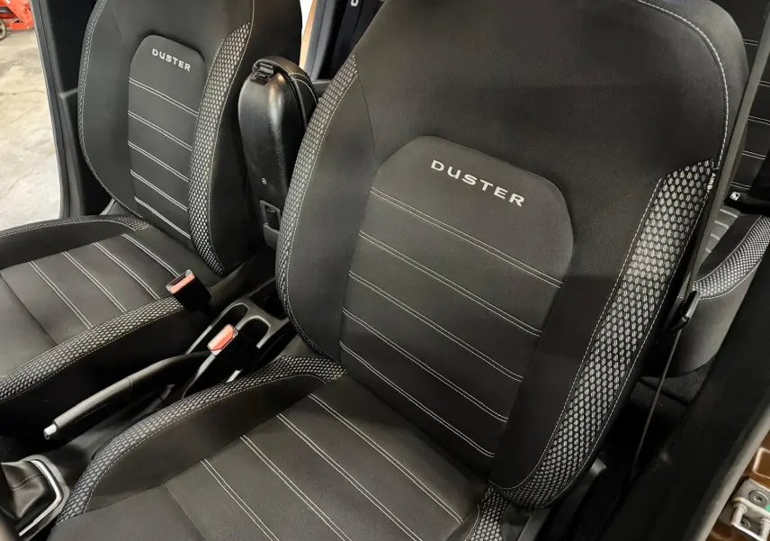 Vue rapprochée des sièges avant noirs du Dacia Duster avec logo DUSTER brodé et console centrale visible.