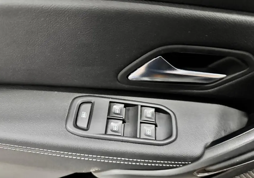 Gros plan sur la commande des vitres électriques et la poignée intérieure en plastique noir du côté gauche du Dacia Duster 2020.