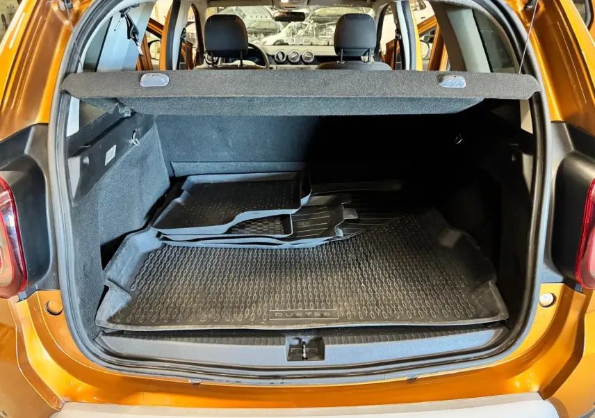 Vue arrière du coffre ouvert d’un Dacia Duster orange 2020 avec tapis de sol en caoutchouc noir.