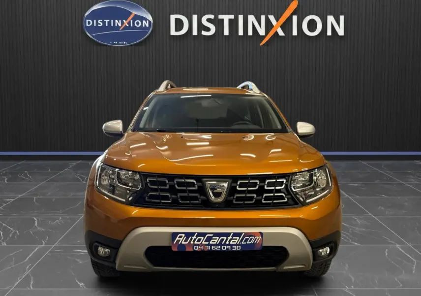 Vue frontale d'un Dacia Duster orange 2020 avec calandre noire et logo au centre, dans un showroom Distinxion.