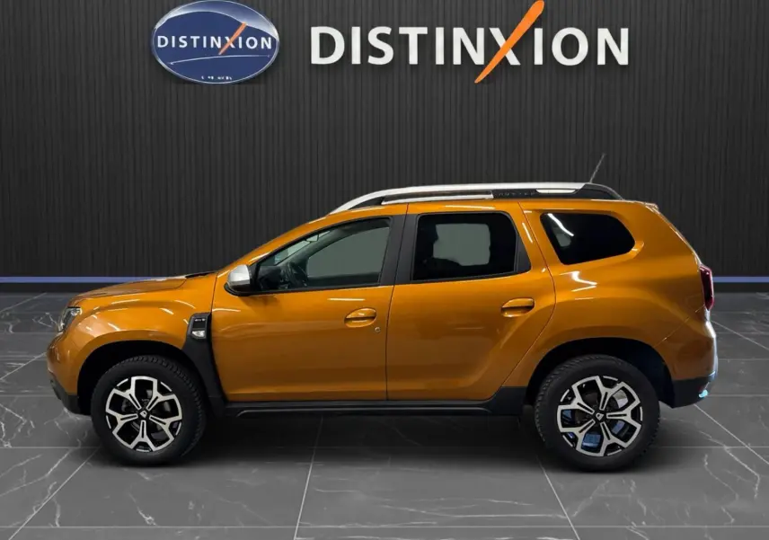 Vue de profil côté gauche d'un Dacia Duster orange 2020 avec jantes bi-ton et barres de toit blanches.