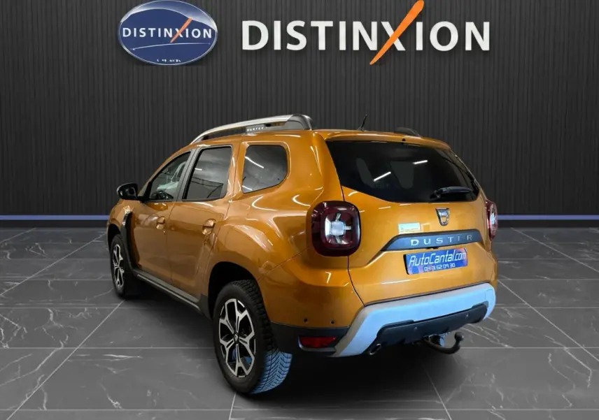 Vue 3/4 arrière droite d'un Dacia Duster orange 2020 avec attelage et jantes bi-ton dans un showroom.