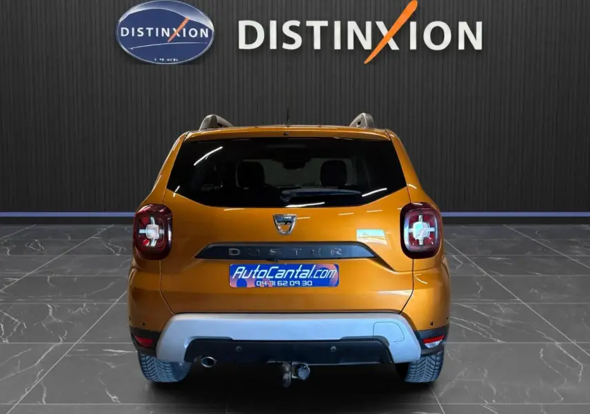 Vue arrière d'un Dacia Duster orange 2020 avec attelage, dans un showroom au sol gris et mur noir marqué Distinxion.