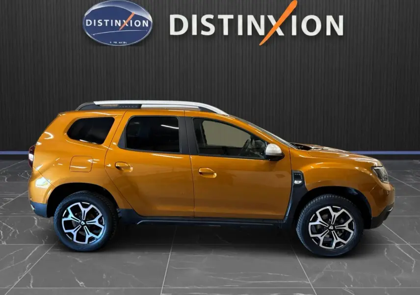 Profil droit d'un Dacia Duster orange 2020 avec jantes bi-ton et barres de toit argentées, sur fond noir Distinxion.