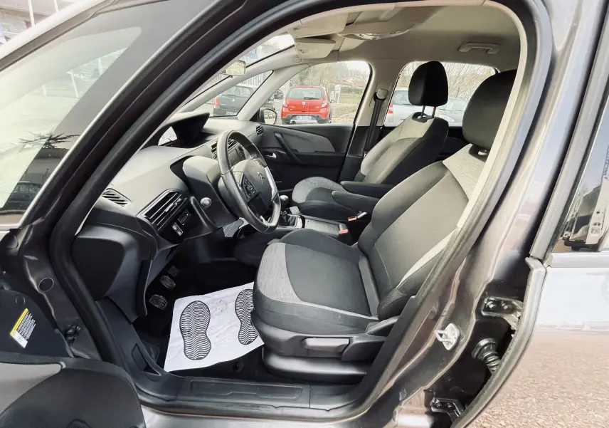 Vue intérieure côté conducteur du Citroën C4 Picasso gris, montrant les sièges tissu noir et gris et le tableau de bord.