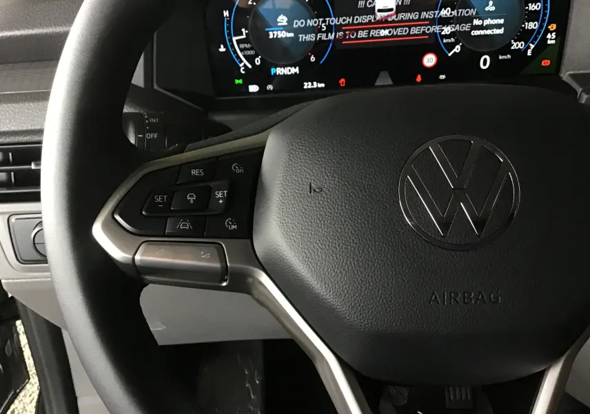 Gros plan sur le volant multifonction noir du Volkswagen Transporter T7 avec tableau de bord numérique en arrière-plan.