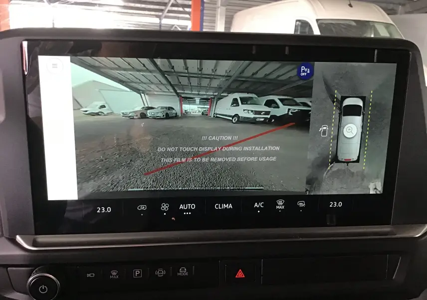 Écran de la caméra 360 affichant une vue arrière et une vue aérienne du Volkswagen Transporter gris anthracite en parking couvert.