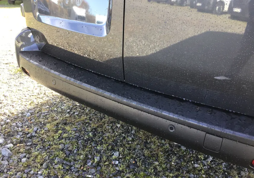 Gros plan sur la partie basse côté droit d'un Citroën Jumpy gris titane avec capteurs de stationnement et gouttes d'eau.