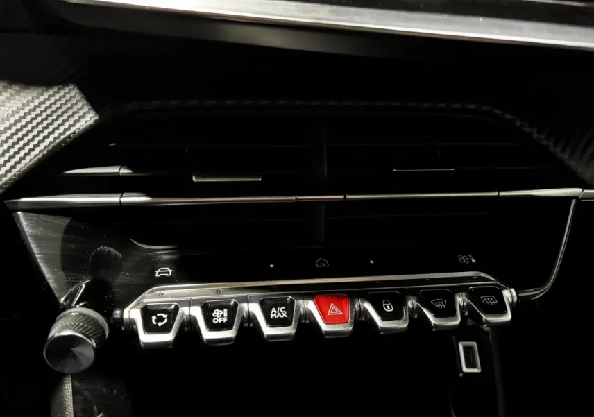 Gros plan sur la rangée de boutons métalliques du tableau de bord du Peugeot 208 gris clair 2024, avec bouton rouge d'alerte au centre.