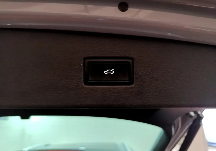 Bouton noir d'ouverture électrique du coffre sur la trappe intérieure d'un Volkswagen Tiguan gris foncé 2021.