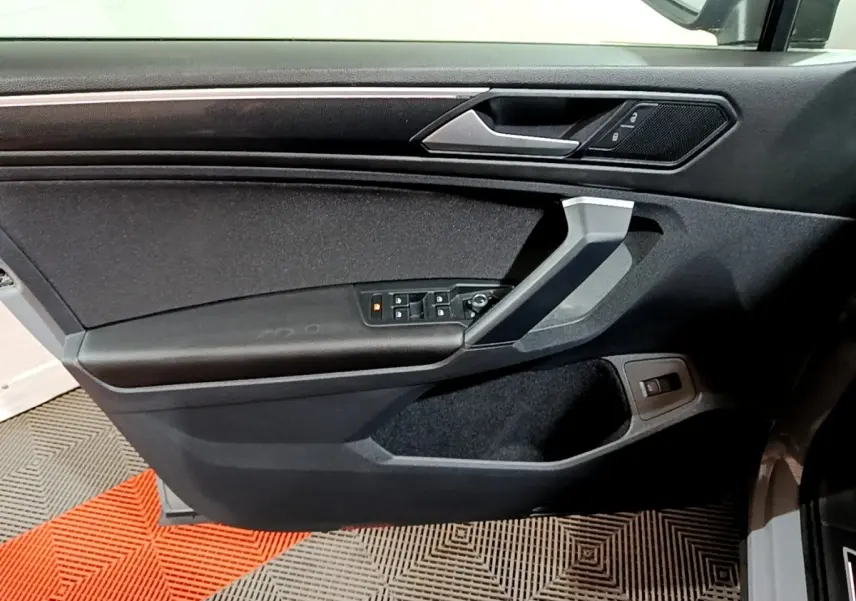 Vue intérieure de la porte côté conducteur du Volkswagen Tiguan gris foncé, avec commandes électriques et poignée argentée.