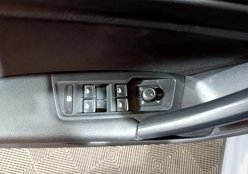 Vue rapprochée des commandes de lève-vitres et réglage des rétroviseurs sur la porte côté conducteur d'un Volkswagen Tiguan gris foncé.