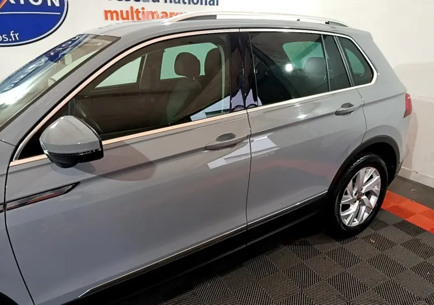 Vue latérale côté gauche d'un Volkswagen Tiguan gris foncé avec rétroviseur et jante alliage visibles.