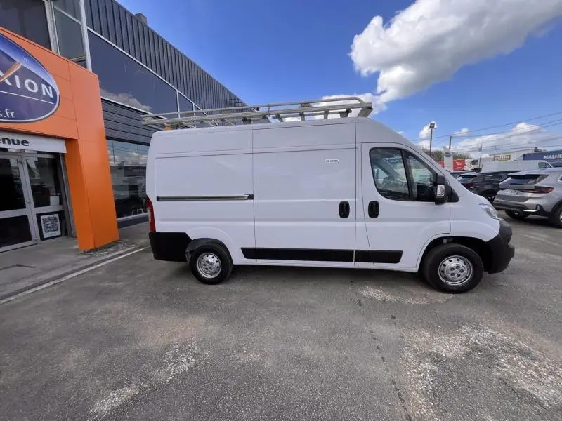 Vue latérale droite d'un Citroën Jumper FGN blanc Icy avec galerie de toit, stationné devant un bâtiment commercial.