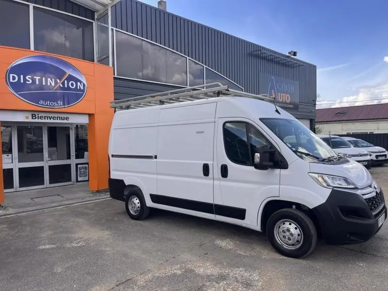 Vue 3/4 avant droit d'un Citroën Jumper blanc Icy avec galerie de toit, stationné devant un bâtiment commercial.