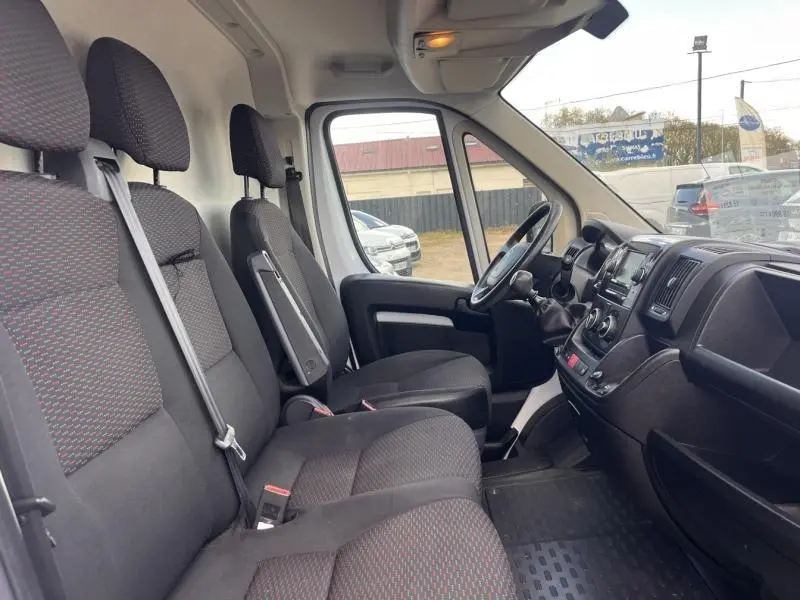 Vue intérieure côté conducteur du Citroën Jumper blanc, montrant les sièges tissu gris foncé et le tableau de bord avec volant multifonction.