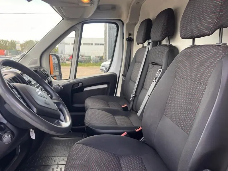 Vue intérieure côté conducteur du Citroën Jumper blanc, montrant les sièges avant en tissu gris foncé avec motifs rouges.