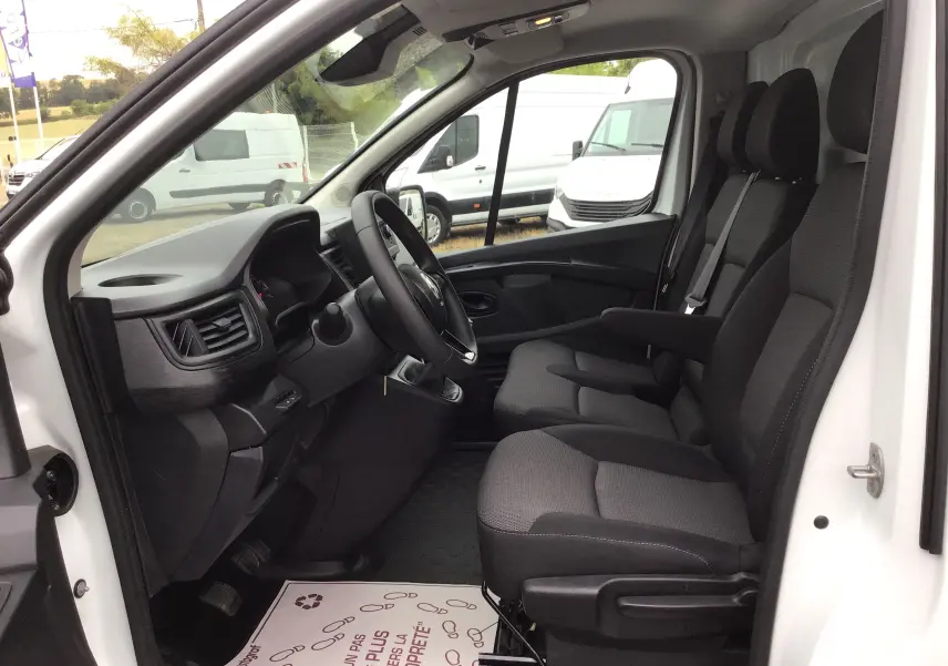 Vue intérieure côté conducteur du Renault Trafic Fourgon blanc 2024, montrant les sièges avant et le tableau de bord.