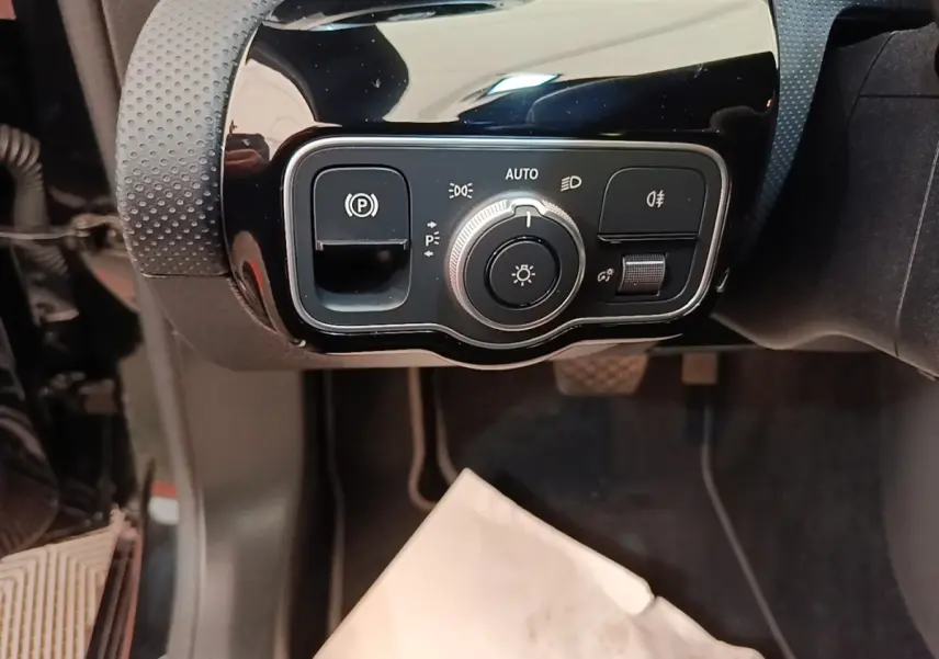 Gros plan sur les commandes d’éclairage et frein à main électrique dans une Mercedes Classe A noire, côté gauche.