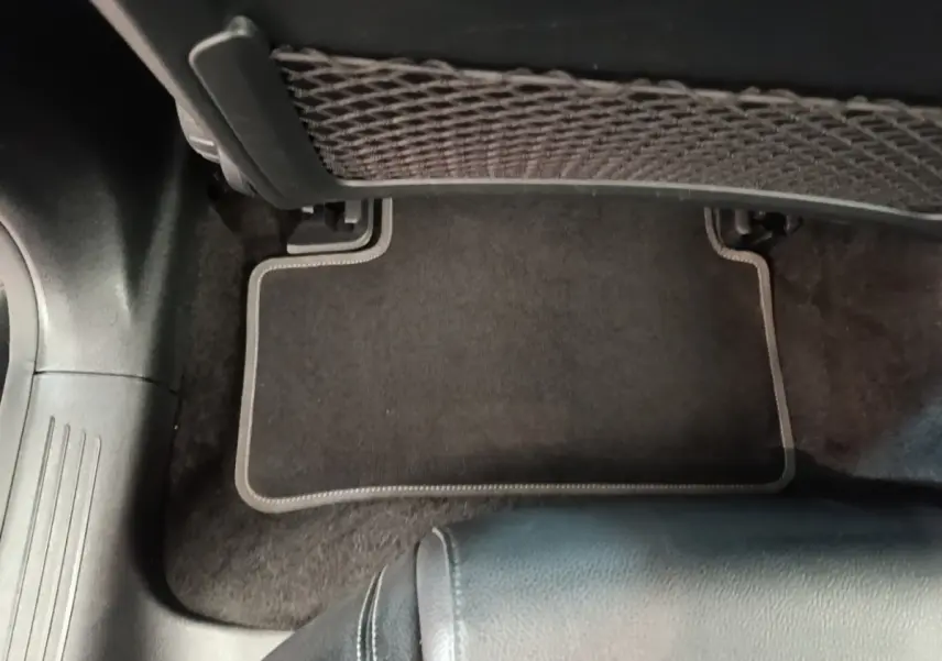 Détail du tapis de sol noir et du filet de rangement sous le siège arrière d'une Mercedes Classe A 250 e 2023.