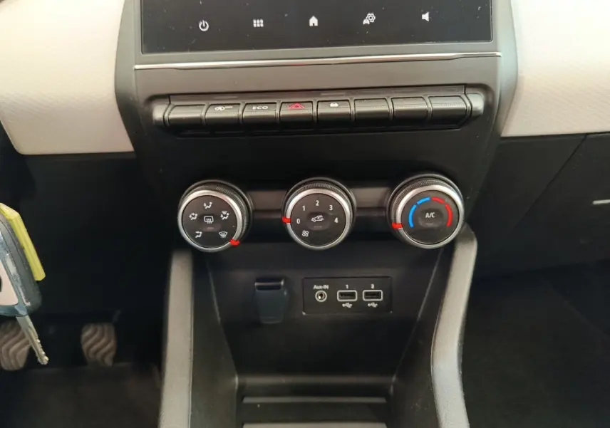 Vue rapprochée du tableau de bord central de la Renault Clio blanche 2023, avec commandes de climatisation et ports USB visibles.