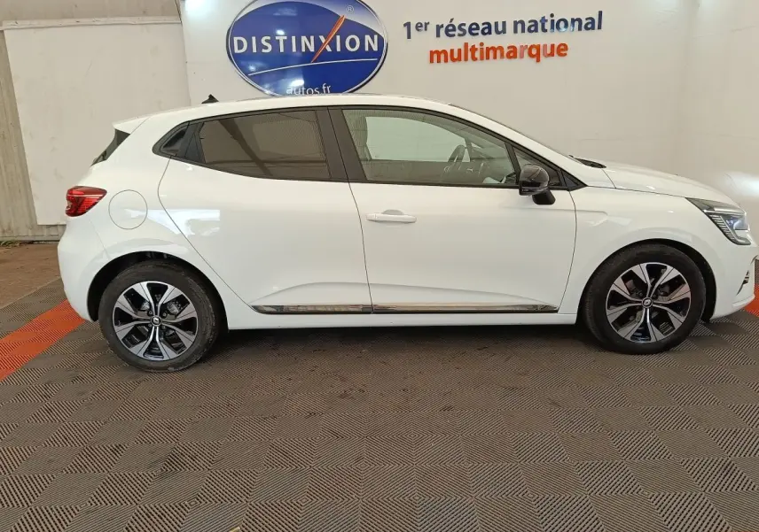 Profil droit d'une Renault Clio blanche 2023 garée en intérieur, avec jantes alliage et rétroviseurs noirs.