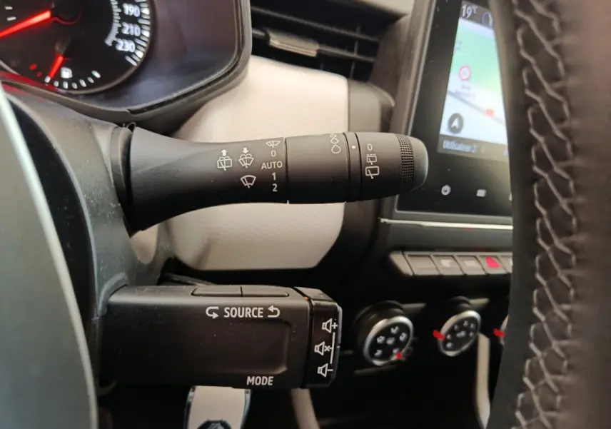 Gros plan sur la commande d’essuie-glace et le volant cuir synthétique de la Renault Clio blanche, avec écran tactile en arrière-plan.