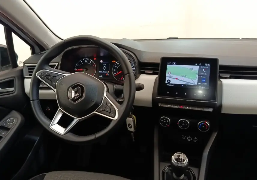 Vue intérieure avant de la Renault Clio blanche 2023, volant multifonctions, écran tactile navigation et levier de vitesse manuel.