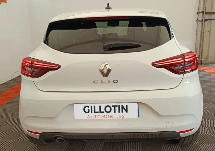 Vue arrière d'une Renault Clio blanche 2023 avec feux LED et spoiler de toit visible en intérieur.