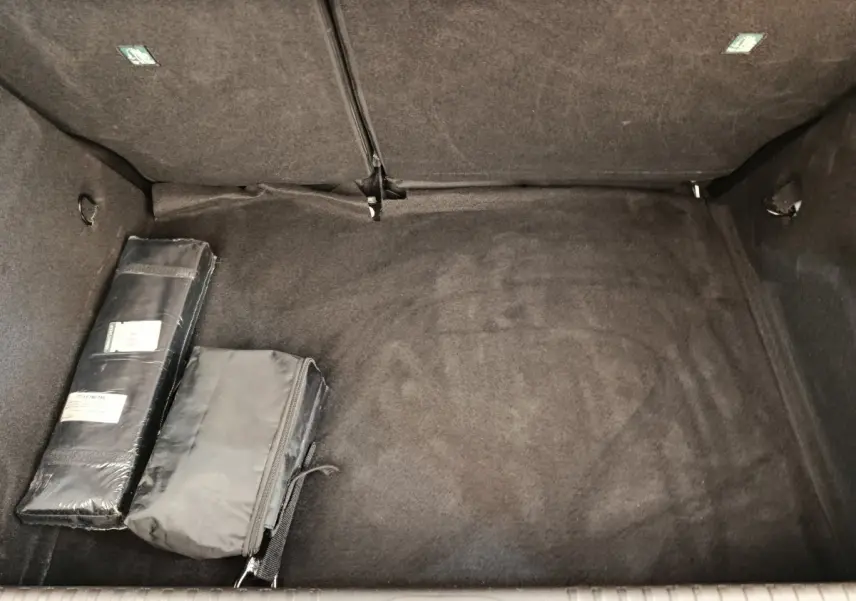 Coffre ouvert de Renault Clio blanc, vue intérieure montrant le tapis noir et deux sacs de rangement.