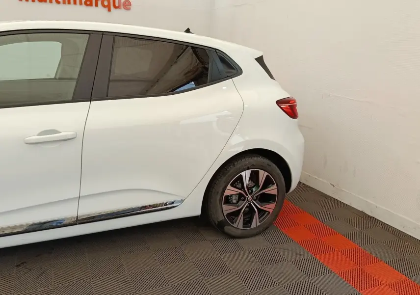 Vue latérale droite sur l'arrière d'une Renault Clio blanche avec jante alliage et baguette chromée basse.