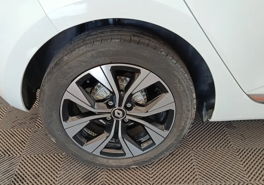Gros plan sur la roue arrière droite d'une Renault Clio blanche avec jante alliage bicolore au design moderne.