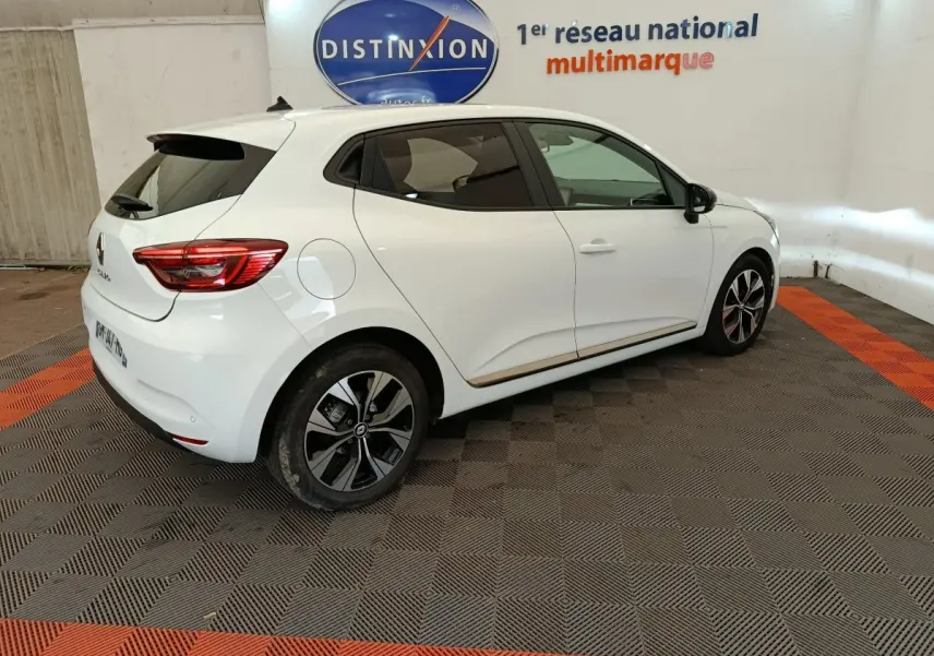 Renault Clio blanc vue 3/4 arrière droit, avec jantes noires et toit avec spoiler, en intérieur showroom.