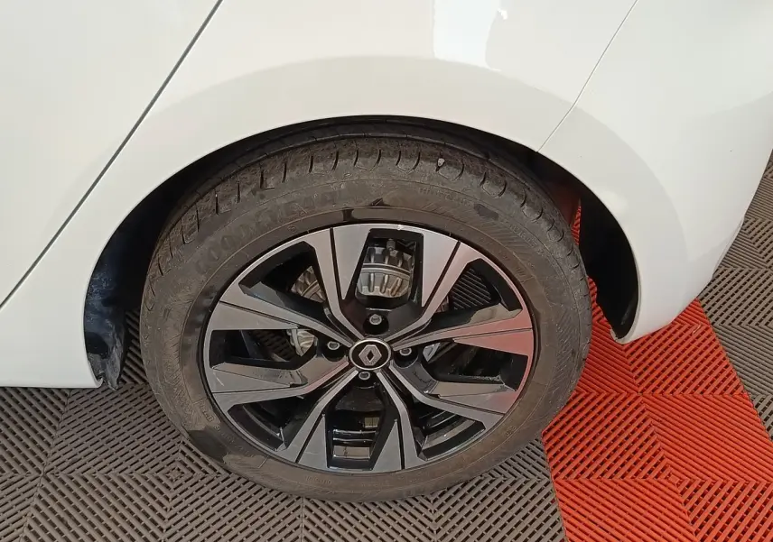 Gros plan sur la roue arrière droite d'une Renault Clio blanche, jante alliage noire au design moderne.