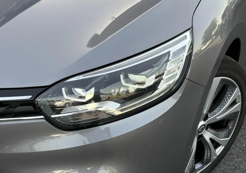 Gros plan sur le phare avant droit et la jante alliage du Renault Grand Scenic IV gris Cassiopée.