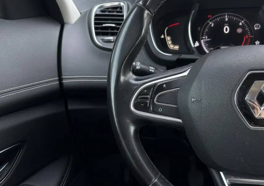 Gros plan sur le volant cuir noir et le tableau de bord digital du Renault Grand Scenic IV, ambiance intérieure sombre.