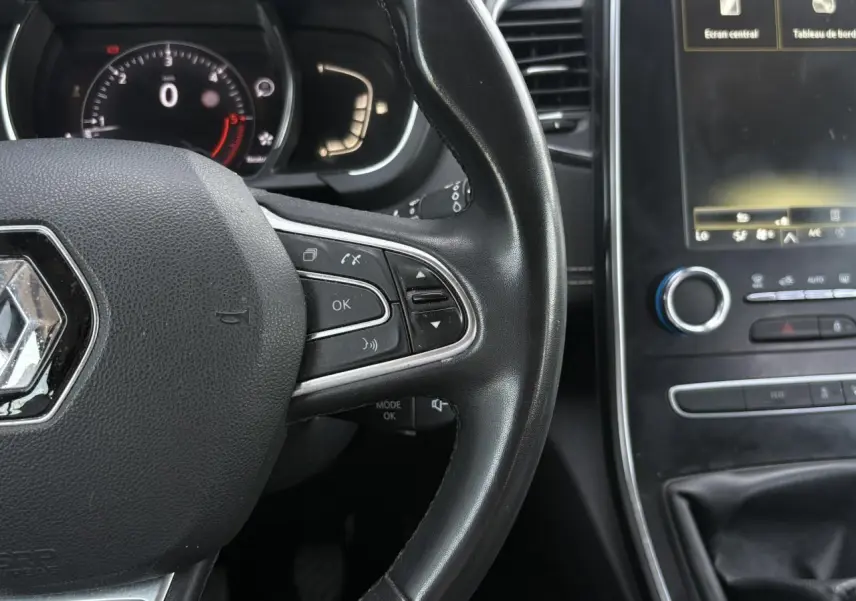 Vue rapprochée du volant cuir noir de la Renault Grand Scenic IV avec commandes intégrées et tableau de bord numérique.